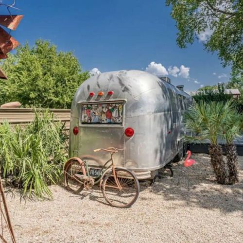 The Airstream is surrounded by shady trees and leafy landscaping